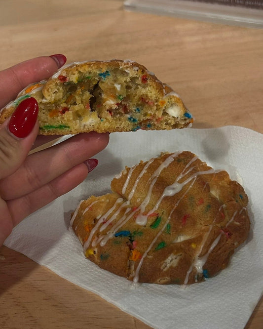 Person holding a colorful cookie with a bite taken out on a wooden surface.
